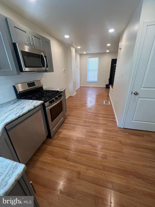 kitchen featuring light hardwood / wood-style flooring, gray cabinets, tasteful backsplash, light stone countertops, and stainless steel appliances