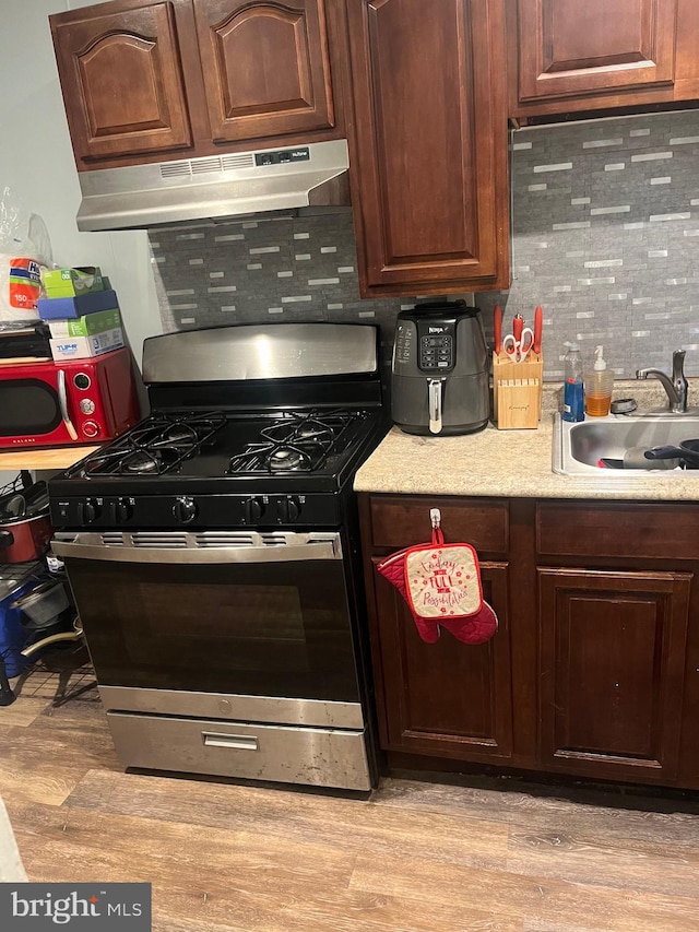 kitchen with sink, decorative backsplash, stainless steel gas stove, and light wood-type flooring