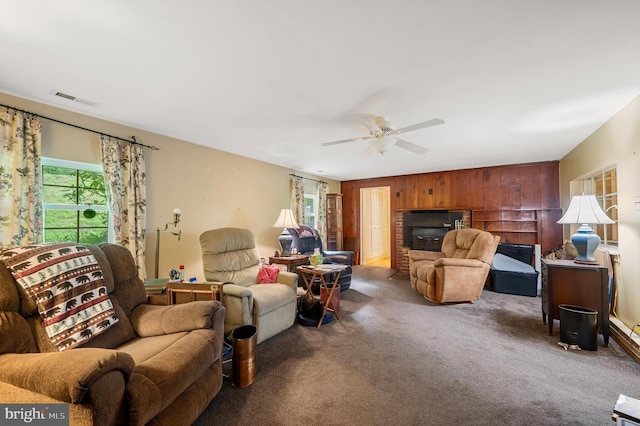 carpeted living room with ceiling fan, a fireplace, and wood walls