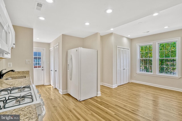 kitchen with white cabinetry, white appliances, light hardwood / wood-style flooring, light stone counters, and sink