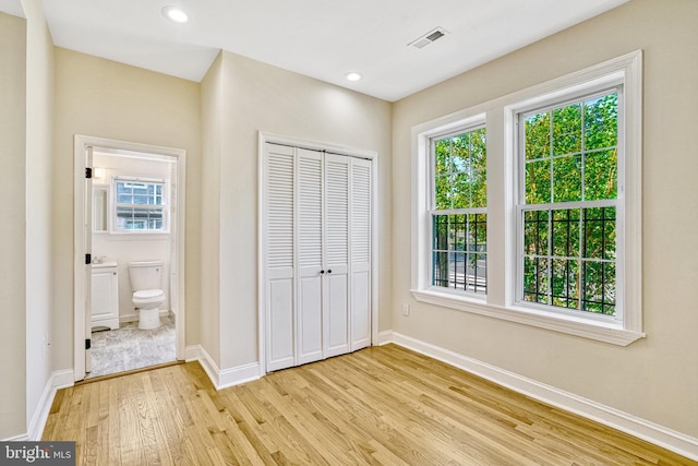 unfurnished bedroom with light hardwood / wood-style flooring, connected bathroom, and a closet