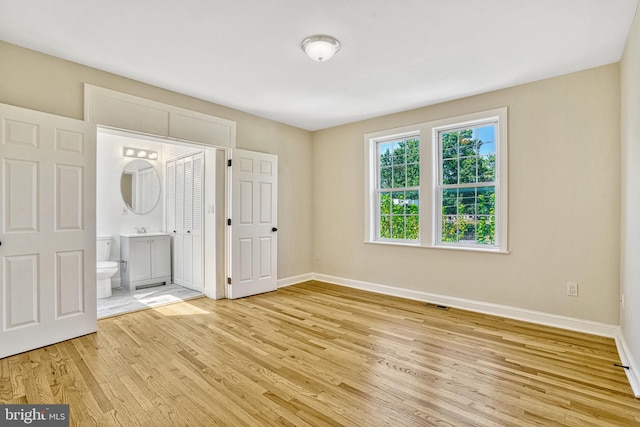 unfurnished bedroom featuring light wood-type flooring, sink, and ensuite bath