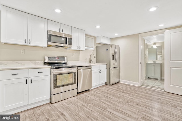 kitchen with stainless steel appliances, sink, white cabinetry, and light hardwood / wood-style floors