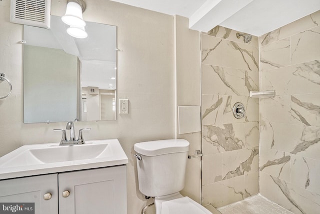 bathroom featuring tiled shower, toilet, and vanity