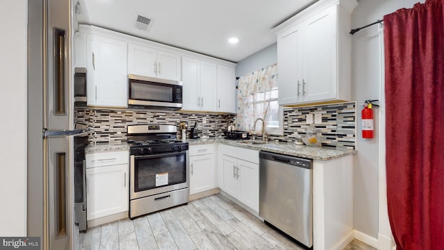 kitchen with tasteful backsplash, light stone countertops, white cabinets, and appliances with stainless steel finishes