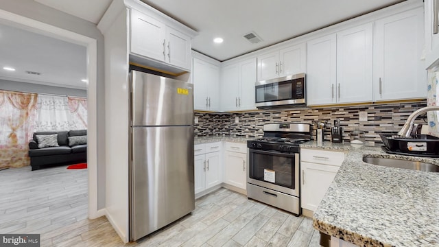 kitchen with light stone counters, stainless steel appliances, sink, and white cabinets