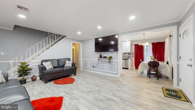 living room featuring light hardwood / wood-style flooring, a chandelier, and ornamental molding