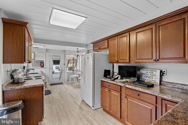 kitchen with dark stone countertops, white refrigerator with ice dispenser, and light wood-type flooring