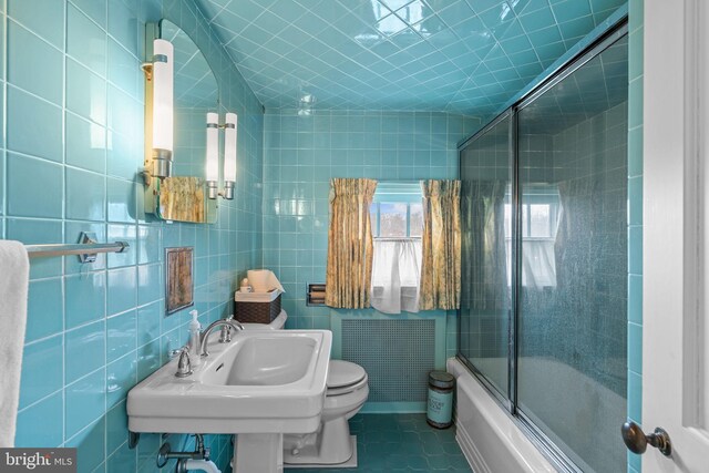 full bathroom featuring toilet, tile walls, combined bath / shower with glass door, tile patterned floors, and sink