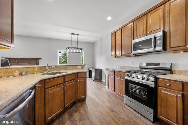 kitchen with dark wood-type flooring, stainless steel appliances, light stone countertops, sink, and decorative light fixtures