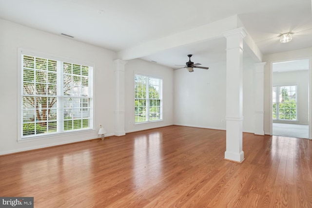 unfurnished living room featuring light wood-type flooring, a healthy amount of sunlight, and ornate columns