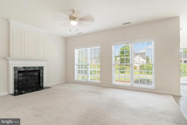 unfurnished living room with a high end fireplace, light colored carpet, and ceiling fan