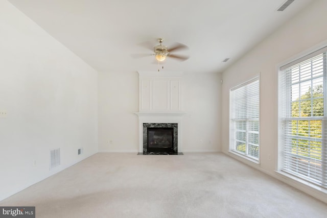 unfurnished living room featuring ceiling fan, plenty of natural light, a high end fireplace, and light carpet