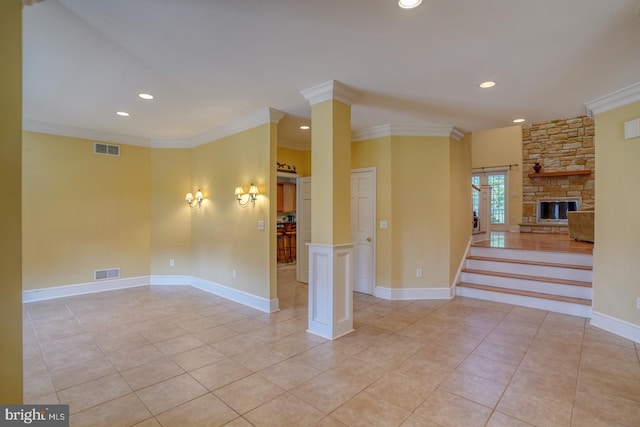 tiled spare room with ornamental molding, a stone fireplace, and ornate columns