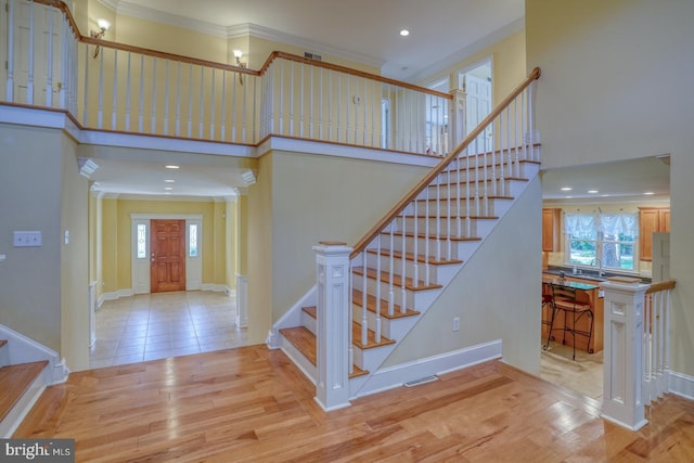 stairway with sink, decorative columns, a high ceiling, wood-type flooring, and ornamental molding