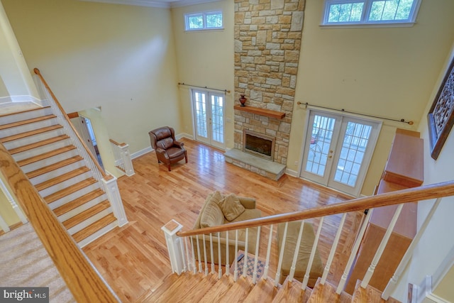 stairway with french doors, a towering ceiling, wood-type flooring, and a stone fireplace