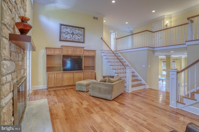 unfurnished living room featuring a fireplace, crown molding, light wood-style flooring, a high ceiling, and stairs