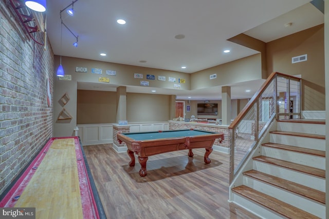 recreation room featuring a wainscoted wall, brick wall, visible vents, light wood-style floors, and track lighting