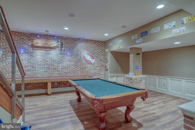 rec room with a decorative wall, recessed lighting, brick wall, wood finished floors, and wainscoting