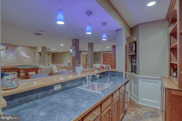 kitchen with wainscoting, open floor plan, pendant lighting, a sink, and a decorative wall