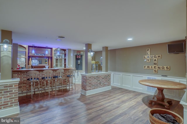 interior space featuring a wainscoted wall, visible vents, a decorative wall, a bar, and wood finished floors