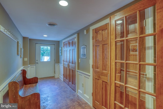 doorway featuring visible vents, a decorative wall, and wainscoting