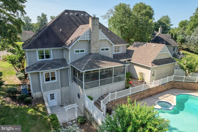 back of house with a fenced backyard, a pool with connected hot tub, a sunroom, roof with shingles, and a chimney