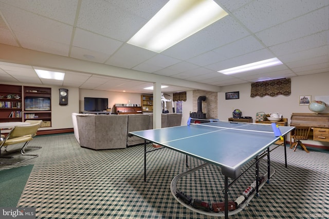 playroom featuring a paneled ceiling, a wood stove, and carpet flooring