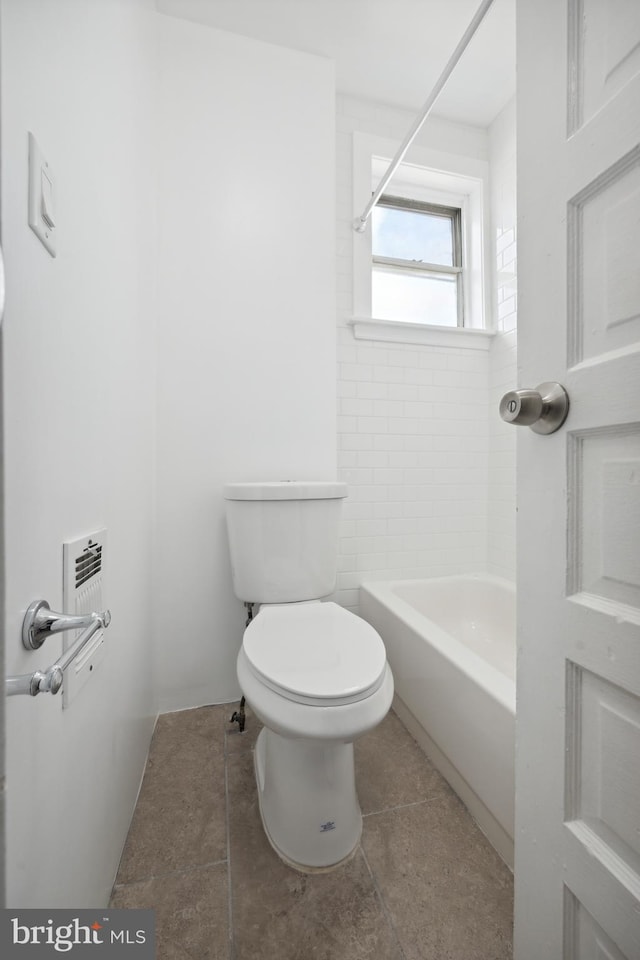 bathroom with toilet, tiled shower / bath combo, and tile patterned flooring