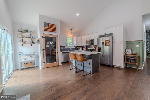 kitchen featuring a kitchen island, appliances with stainless steel finishes, white cabinets, dark hardwood / wood-style flooring, and a kitchen bar