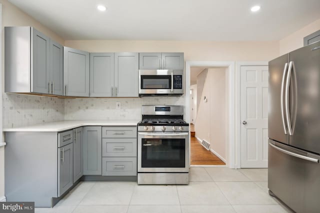 kitchen featuring backsplash, gray cabinets, light tile patterned flooring, and appliances with stainless steel finishes