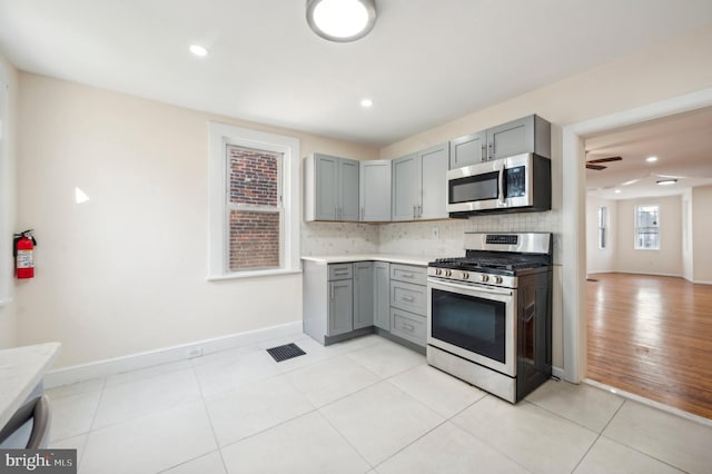 kitchen featuring tasteful backsplash, appliances with stainless steel finishes, light tile patterned floors, and gray cabinetry