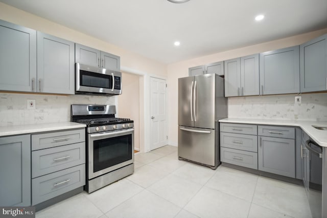 kitchen with stainless steel appliances, gray cabinets, light tile patterned floors, and decorative backsplash