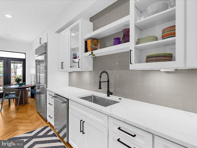 kitchen with light parquet flooring, white cabinets, sink, light stone countertops, and appliances with stainless steel finishes