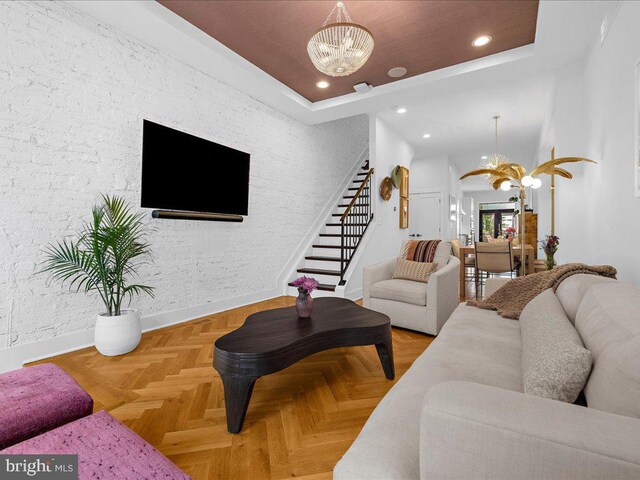 living room with light parquet floors, an inviting chandelier, and a raised ceiling