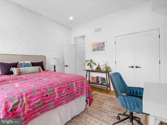 bedroom with brick wall, light hardwood / wood-style flooring, and a closet