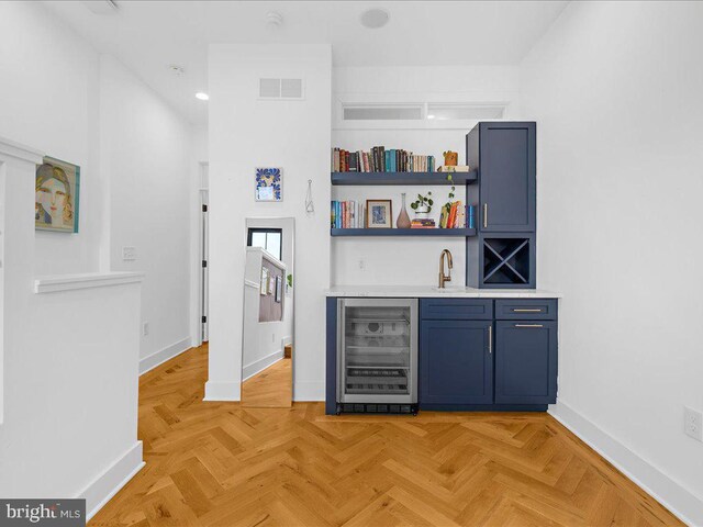 bar featuring sink, blue cabinetry, light parquet flooring, and beverage cooler