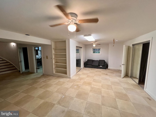 finished below grade area featuring built in shelves, a ceiling fan, stairs, and baseboards