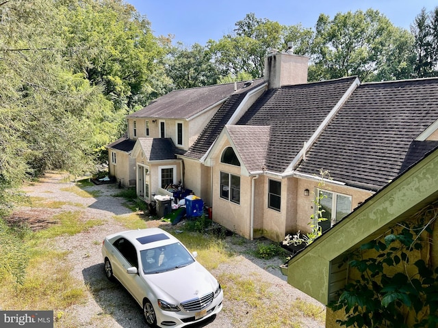 exterior space with stucco siding, a chimney, and roof with shingles