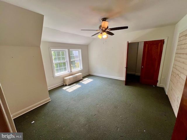 unfurnished bedroom featuring lofted ceiling, a ceiling fan, radiator, dark colored carpet, and baseboards