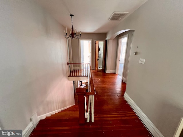 hall with visible vents, hardwood / wood-style flooring, arched walkways, baseboards, and a chandelier