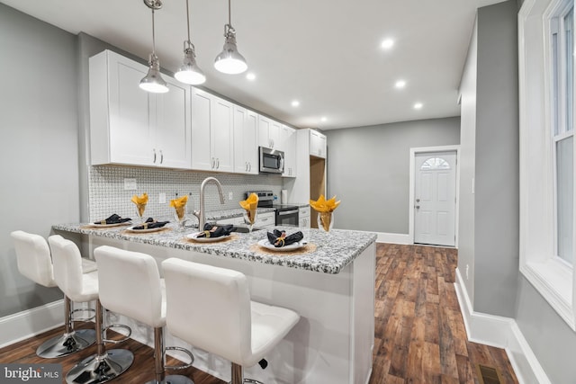 kitchen with sink, appliances with stainless steel finishes, kitchen peninsula, light stone countertops, and white cabinets