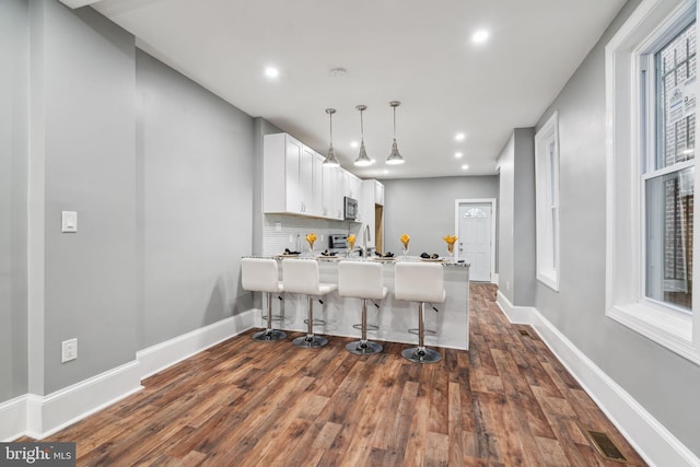 kitchen featuring a breakfast bar area, white cabinetry, hanging light fixtures, tasteful backsplash, and kitchen peninsula