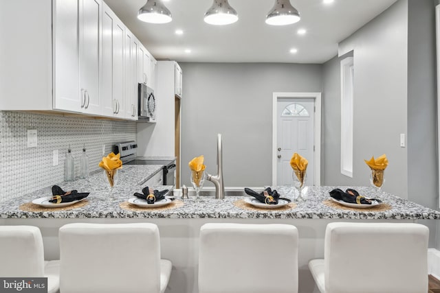 kitchen featuring appliances with stainless steel finishes, white cabinetry, backsplash, a kitchen bar, and light stone countertops