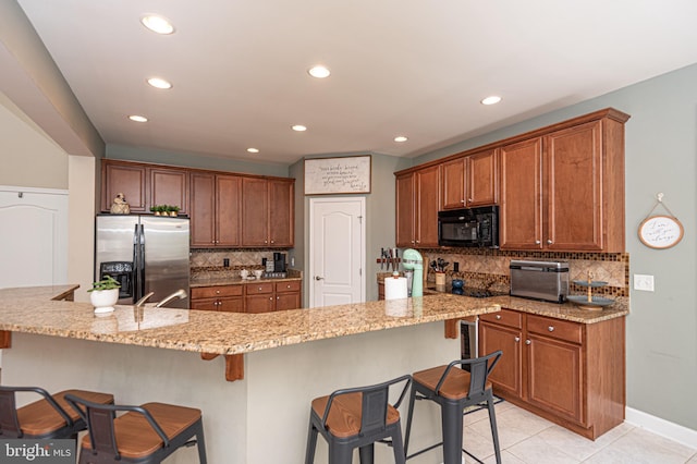 kitchen featuring brown cabinets, black microwave, stainless steel fridge, and a breakfast bar area