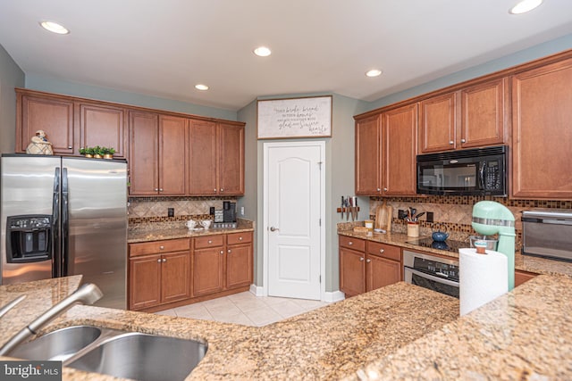 kitchen with stainless steel appliances, light tile patterned floors, a sink, and light stone countertops