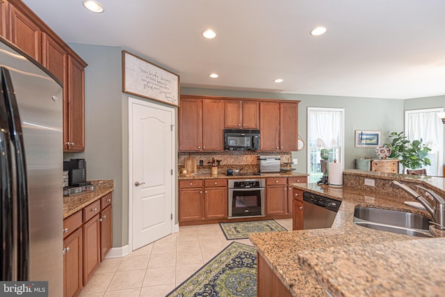 kitchen with light stone counters, a sink, appliances with stainless steel finishes, backsplash, and brown cabinetry