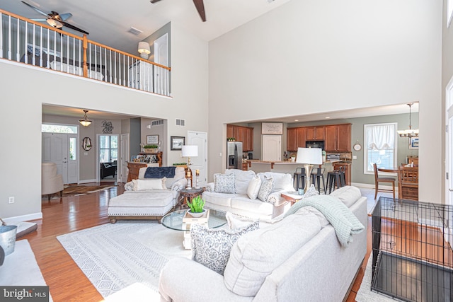 living area featuring light wood-style flooring, visible vents, baseboards, and ceiling fan with notable chandelier