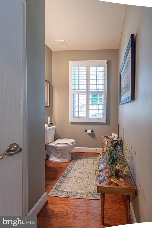 half bathroom with toilet, wood finished floors, visible vents, and baseboards