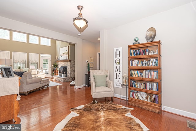 sitting room featuring a stone fireplace, wood finished floors, visible vents, and baseboards